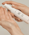Hand holding a white skincare bottle with visible brand name on a neutral background