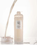 Bottle of skincare product with a label, surrounded by splashes of liquid on a white background