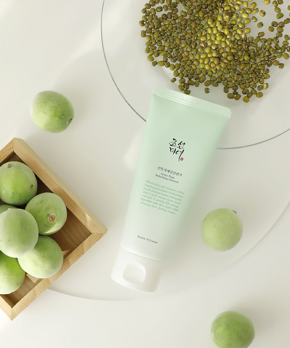 Green skincare product with green beans and plums on a white background