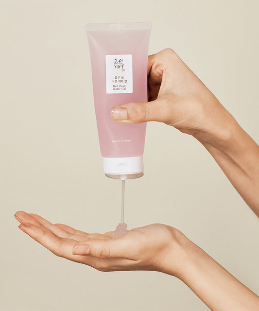 Hand holding a pink tube of skincare product with a beige background