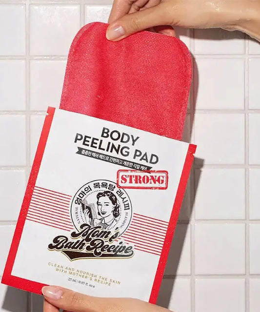 Red body peeling pad with 'Mom Bath Recipe' packaging held against a tiled wall background.