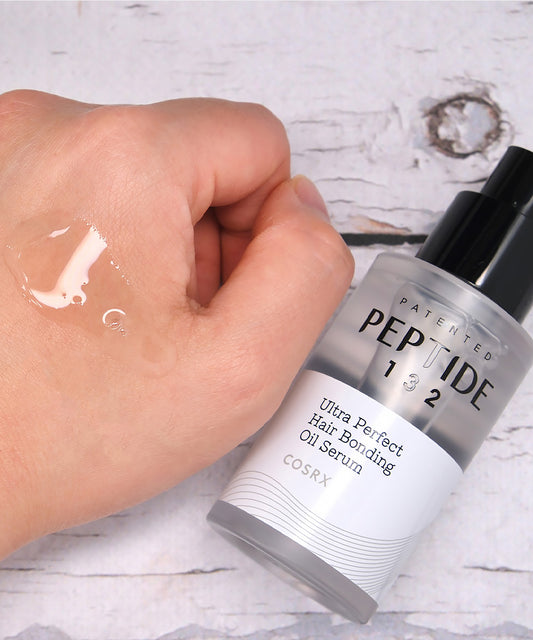 CosRX Peptide 132 Ultra Perfect Hair Bending Oil Serum being applied to a hand on a light background