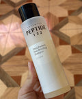CosRX Peptide 132 shampoo bottle held in a hand with a geometric patterned background