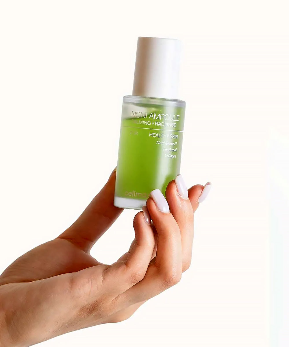 Hand holding a green skincare bottle with a white cap on a white background