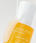 Bottle of dark spot serum with a white cap on a light gray background