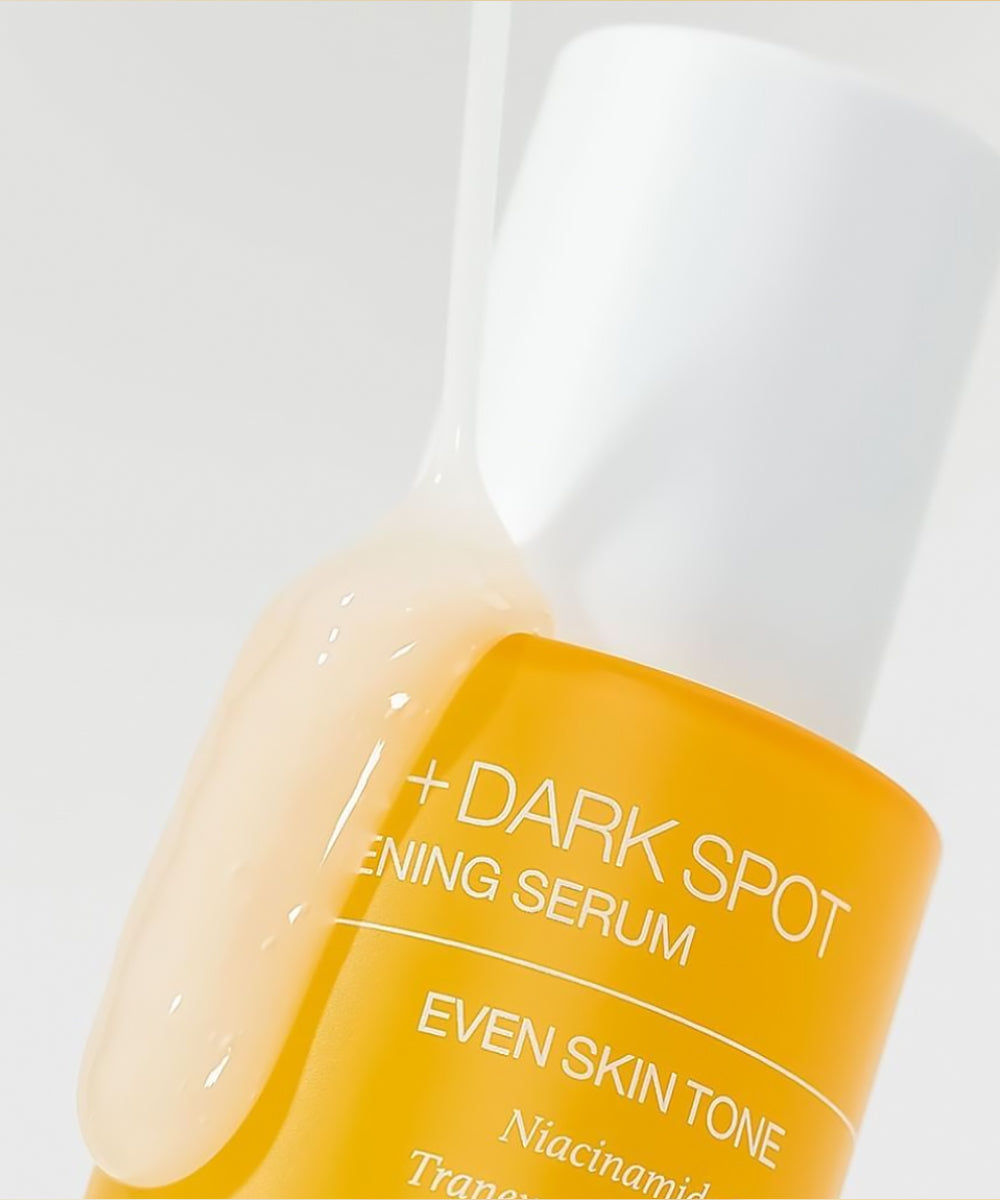Bottle of dark spot serum with a white cap on a light gray background