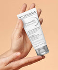 Hand holding a Bioderma skincare product against a beige background