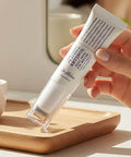 Close-up of a hand holding the Dr. Althea Retinol Eye Roller over a wooden vanity tray, highlighting the sleek, ergonomic design for targeted under-eye application