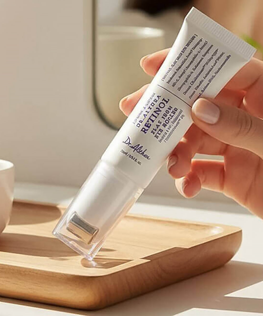 Close-up of a hand holding the Dr. Althea Retinol Eye Roller over a wooden vanity tray, highlighting the sleek, ergonomic design for targeted under-eye application