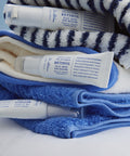 Lifestyle photography of three Dr. Althea Retinol Flat Iron Eye Roller tubes resting on plush blue and white striped bathroom towels, emphasizing a clean and refreshing skincare routine