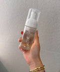 Hand holding a skincare bottle with a plain background
