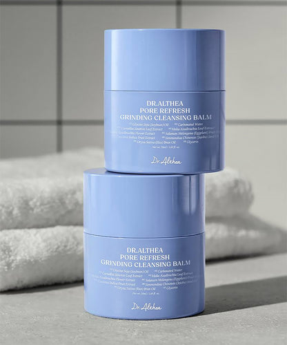Two blue containers of Dr. Althea Pore Refresh Grinding Cleansing Balm on a gray surface with towels in the background.