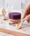 Dr. Melaxin Calcium dark spot cover eye cream with a hand holding a applicator on a marble surface.