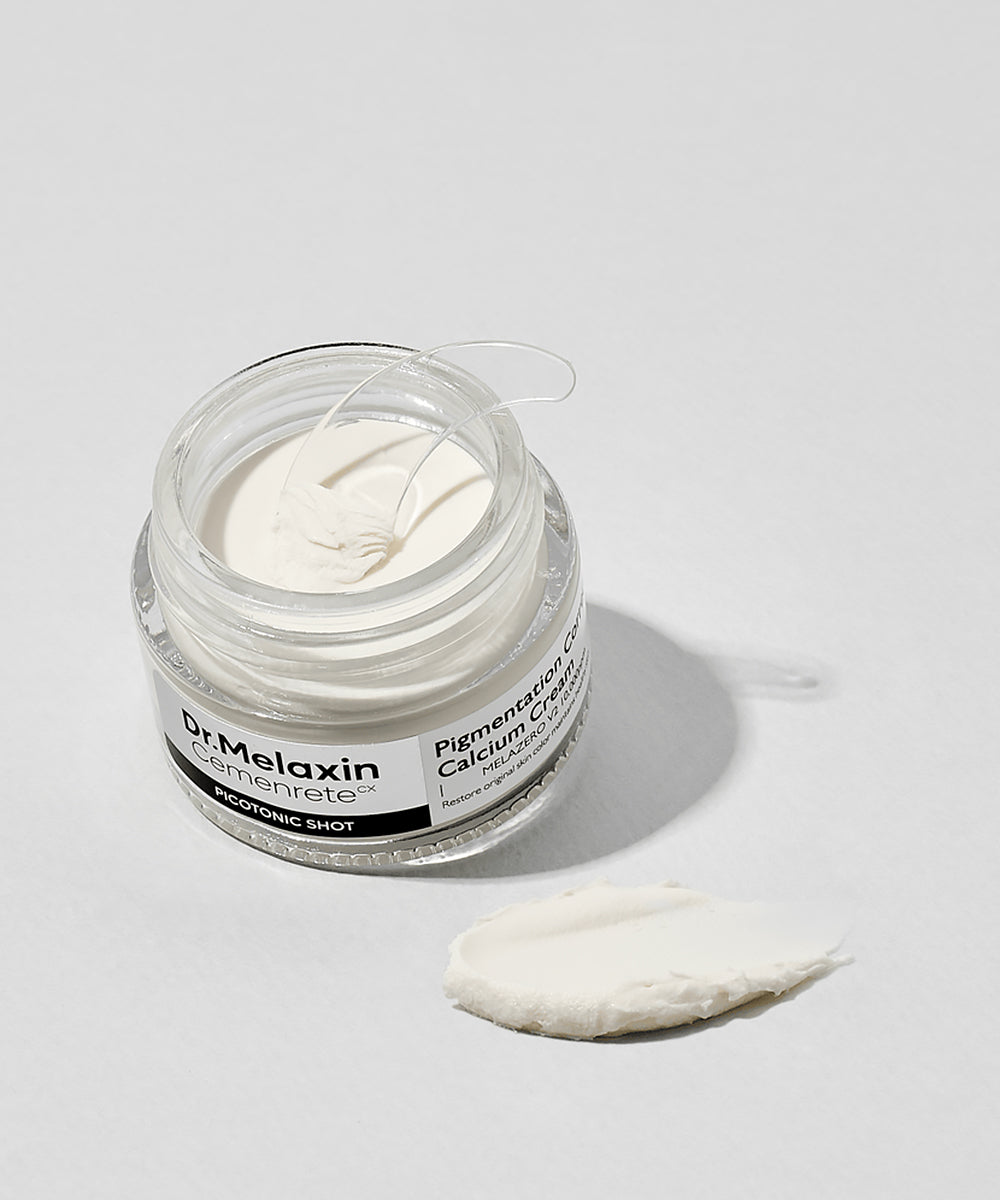An open jar of Dr. Melaxin Pigmentation Corrector with a clear applicator spatula and a swatch of the rich, white cream texture on a plain white surface