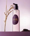 The EQQUALBERRY Purple Rice Pore Smoothing Cleansing Oil standing on a purple pedestal, styled with natural rice stalks and a small mound of purple rice grains to highlight its key ingredients