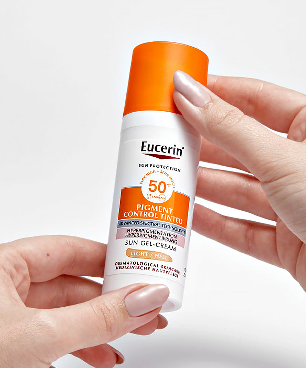 Eucerin sun protection cream bottle held by a hand on a white background
