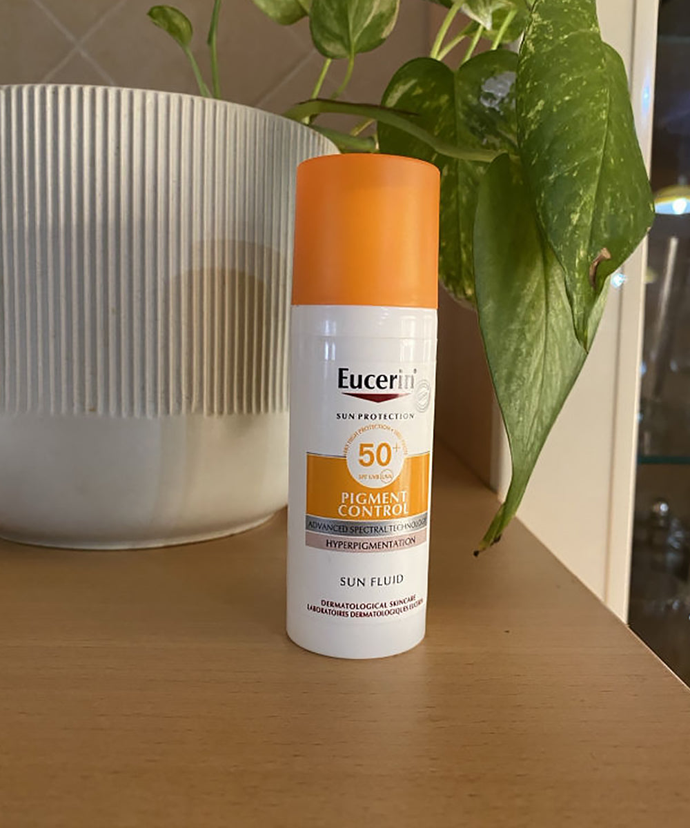 Eucerin sunscreen bottle on a wooden surface with a plant in the background