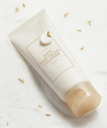 White rice facial cleanser bottle on a light background with scattered rice grains.