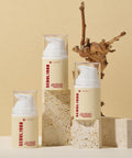Creative product arrangement of three K-SECRET Seoul 1988 Cream pump bottles on rough, natural stone blocks, with a dried branch accent against a warm beige background