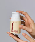 A close-up view of elegant, manicured hands holding the K-SECRET Seoul 1988 Cream pump bottle, with product label details clearly visible against a cool gray background