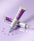 A lifestyle shot showing two silver tubes of Mary & May Spicule Collagen PDRN Cream on a lavender surface, surrounded by small purple cream droplets to showcase product texture