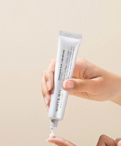 Hand holding a tube of MARY & MAY skincare product against a beige background