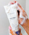 White Collagen Cleansing Foam tube with foam on a hand against a neutral background