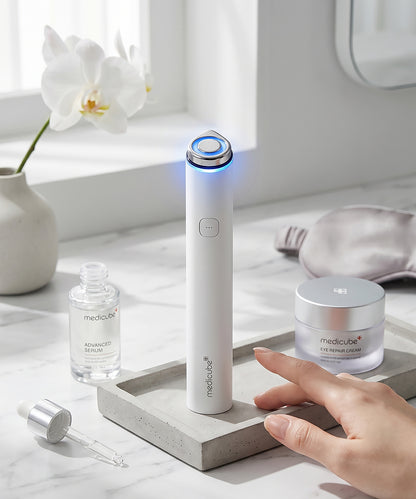 Close-up of the Medicube device being held, showcasing the sleek control buttons and the active LED indicator light on the side of the matte white handle