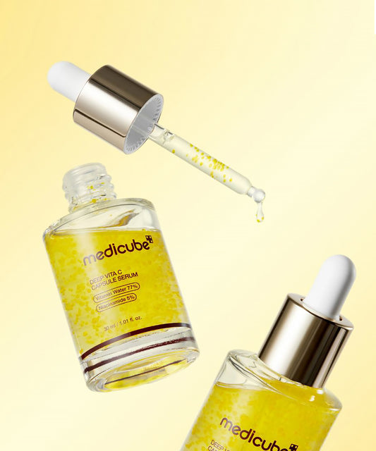 Dropper dispensing the Deep Vita C Serum, showcasing the clear liquid formula suspended with small, bright yellow vitamin capsules