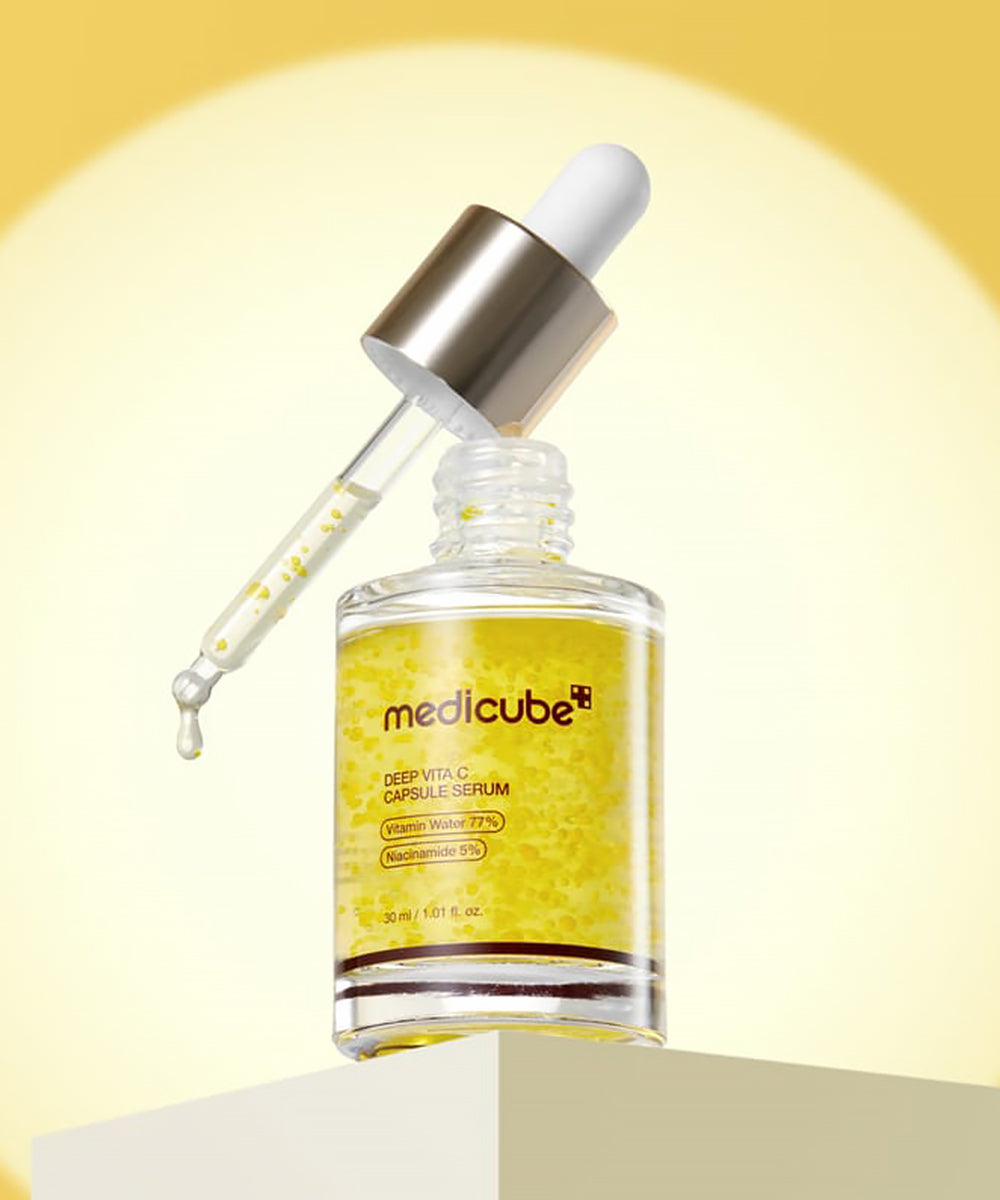 An angled view of the Medicube Deep Vita C Serum bottle with its dropper resting on the rim, positioned on a minimalist light-colored podium