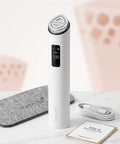 A white and silver Medicube AGE-R Beauty Boosten Pro skincare device stands upright on a light marble surface, with a gray felt case, white charging cable, and instruction booklet arranged around it against a soft pink and white background.