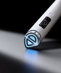A close-up of a white handheld beauty device with a digital display and a glowing blue LED tip, resting on a reflective dark surface against a black background.