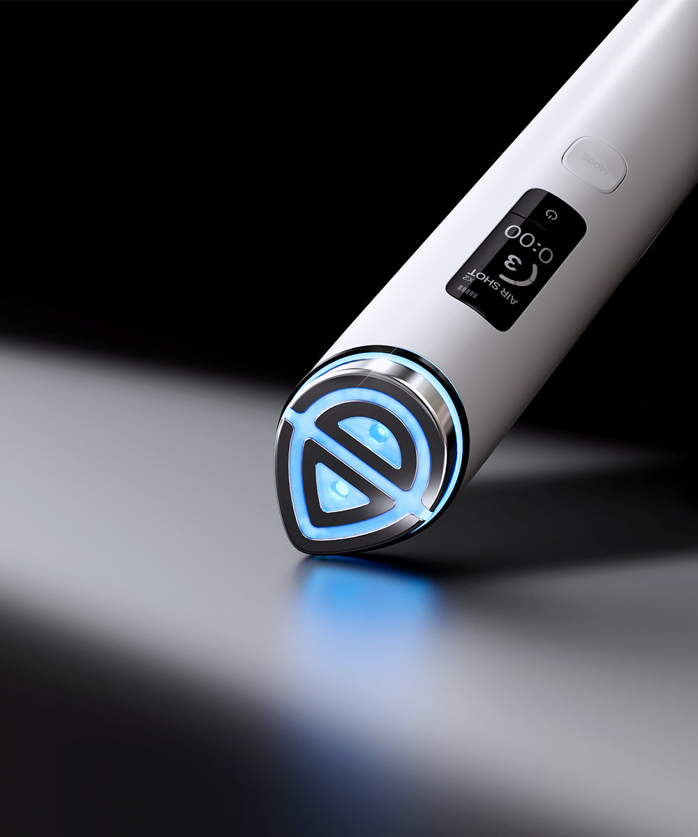 A close-up of a white handheld beauty device with a digital display and a glowing blue LED tip, resting on a reflective dark surface against a black background.