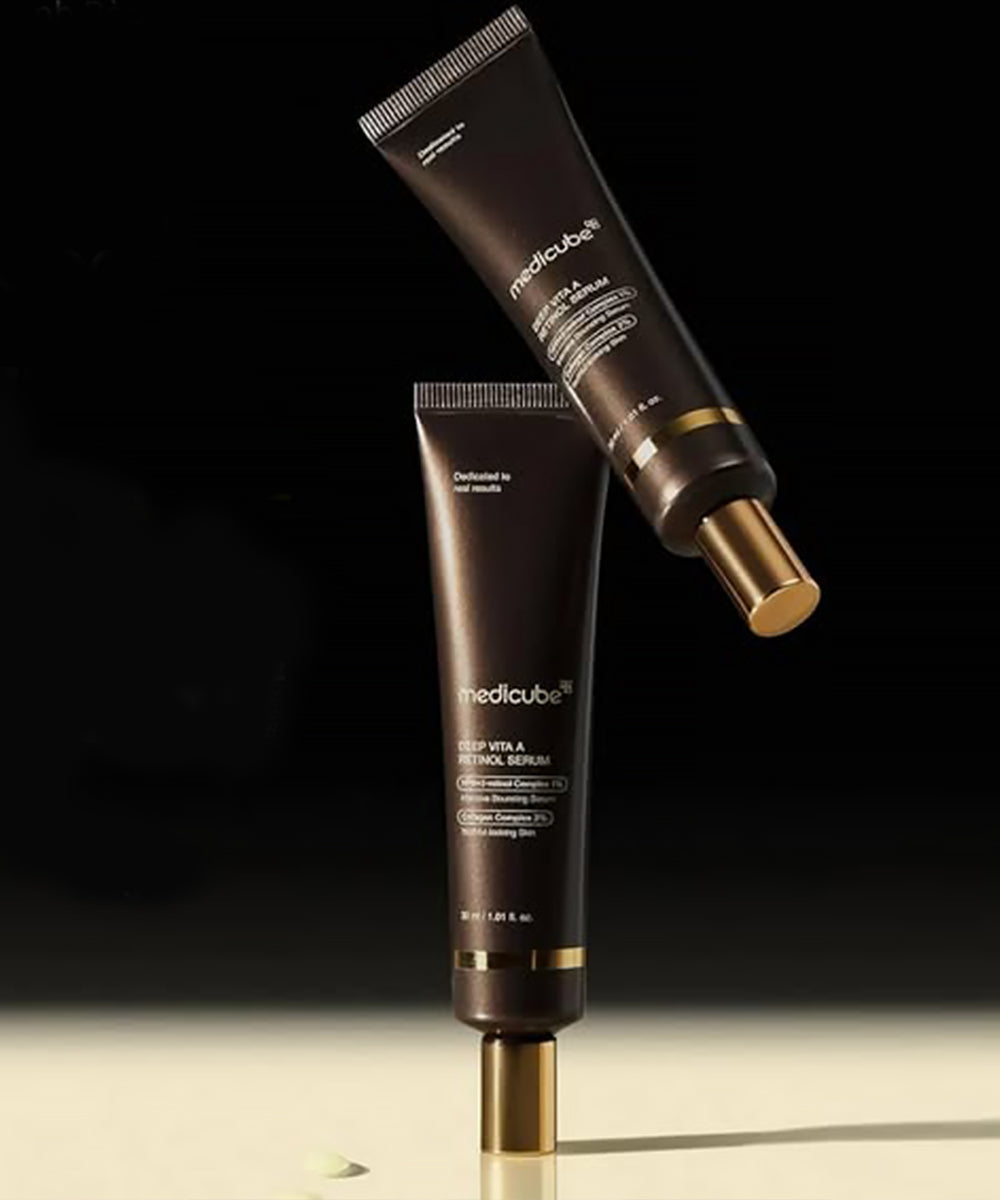 Two dark brown skincare products with gold accents on a reflective surface and black background