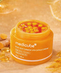 Orange jar of Medicube cream with turmeric capsules on a beige background