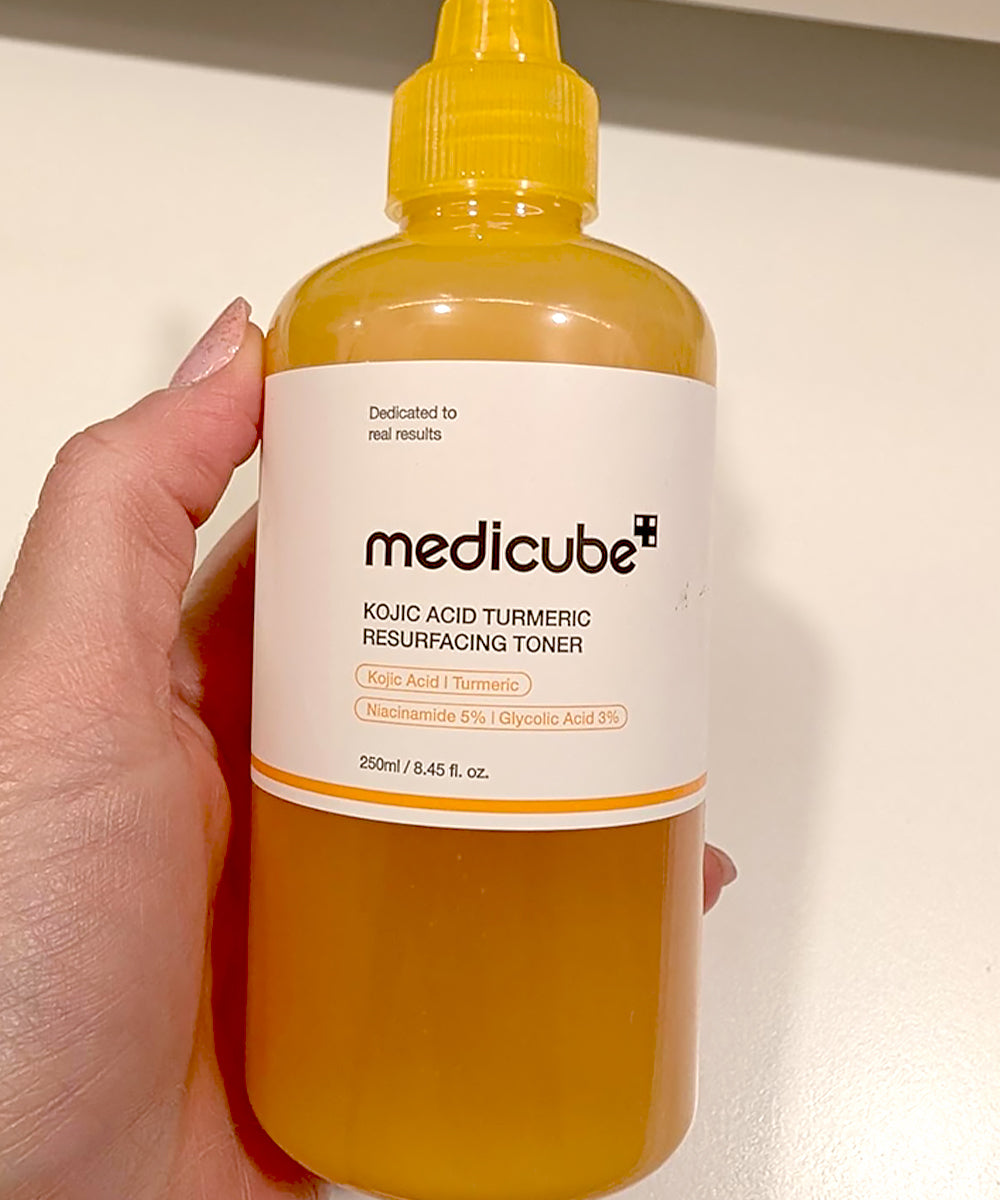 Bottle of Medicube toner held by a hand against a neutral background