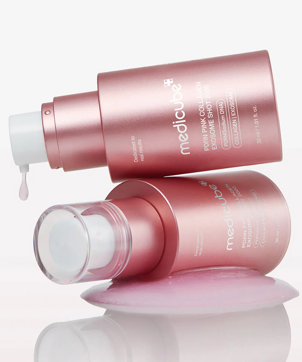 Two Medicube PDRN Pink Collagen Exosome Shot 2000 bottles stacked horizontally, featuring a single droplet of pink serum and a pool of product on a clean white surface