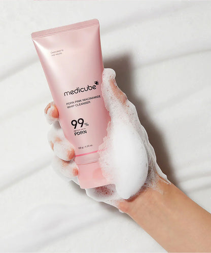 A close-up view of a hand holding the Medicube PDRN Pink Niacinamide Whip Cleanser tube, covered in rich, thick white lather to demonstrate the whipped texture