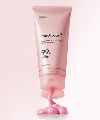 Vertical product shot of the Medicube PDRN Pink Niacinamide Whip Cleanser standing on a pink background, with a dollop of the rich pink cleanser being actively dispensed from the nozzle to showcase its glossy texture