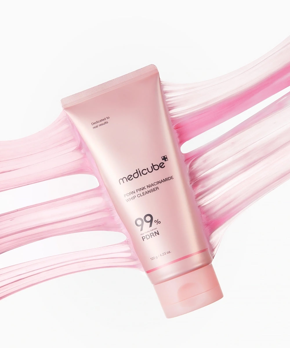 An artistic, top-down product shot of the Medicube PDRN Pink Niacinamide Whip Cleanser tube surrounded by multiple wide, stretching, translucent pink texture swatches on a white background