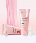 A stylized product composition on a soft pink background, featuring two Medicube PDRN Pink Niacinamide Whip Cleanser tubes—one standing and one lying down—combined with a curtain of pink stretching cleanser and white whipped foam