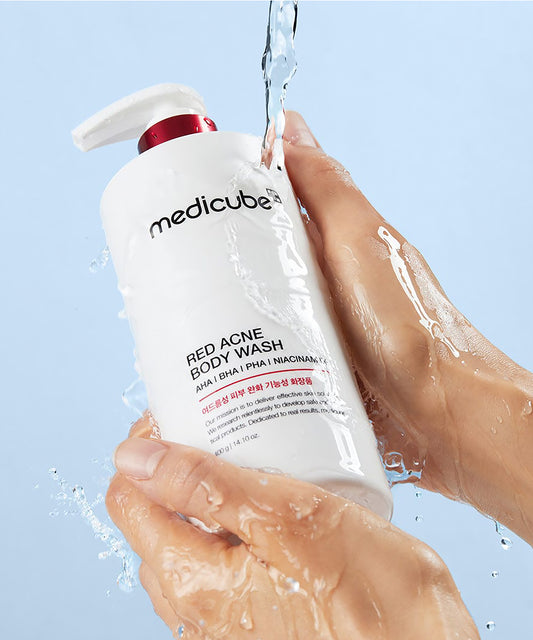 Hand holding a bottle of Medicube Red Acne Body Wash with water droplets on a light blue background