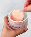 Person using a Medicube skincare product with a cotton pad on a plain background