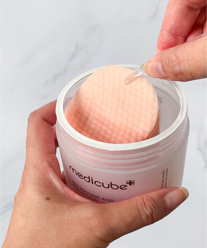 Person using a Medicube skincare product with a cotton pad on a plain background