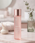 The toner bottle stands on a marble surface in a bright bathroom setting, accompanied by a small vase of eucalyptus and a white towel