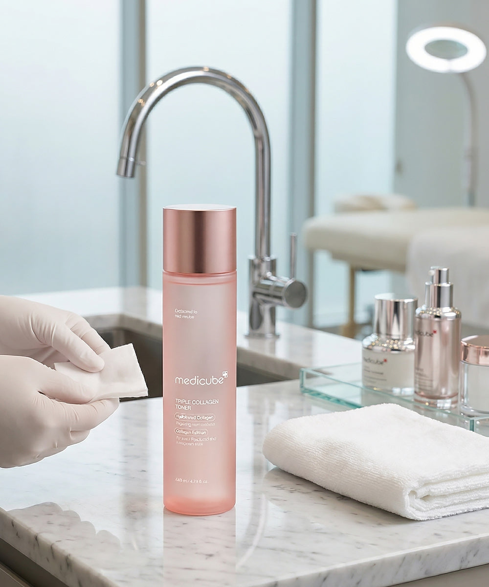 The toner bottle sits on a marble counter in a professional spa or clinic setting, with gloved hands holding a cotton pad in the foreground