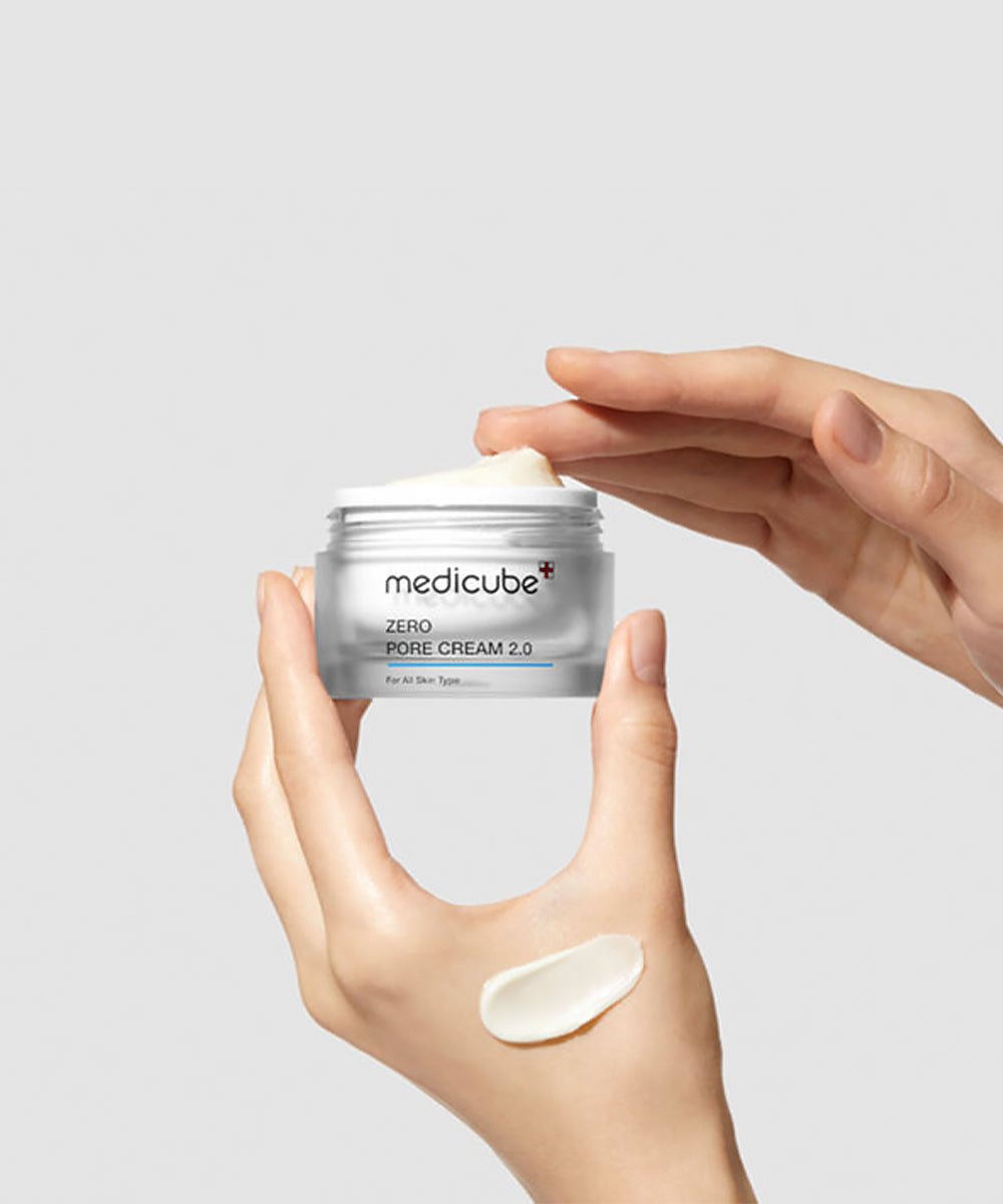 Hand holding a jar of Medicube Zero Pore Cream 2.0 with a small amount on the palm against a light gray background.