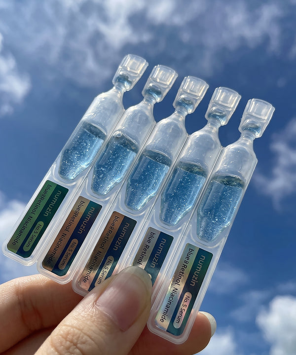 A hand using the glass dropper to dispense the Numbuzin Blue Bio-Retinol Serum, highlighting its lightweight, translucent blue liquid texture designed for quick absorption