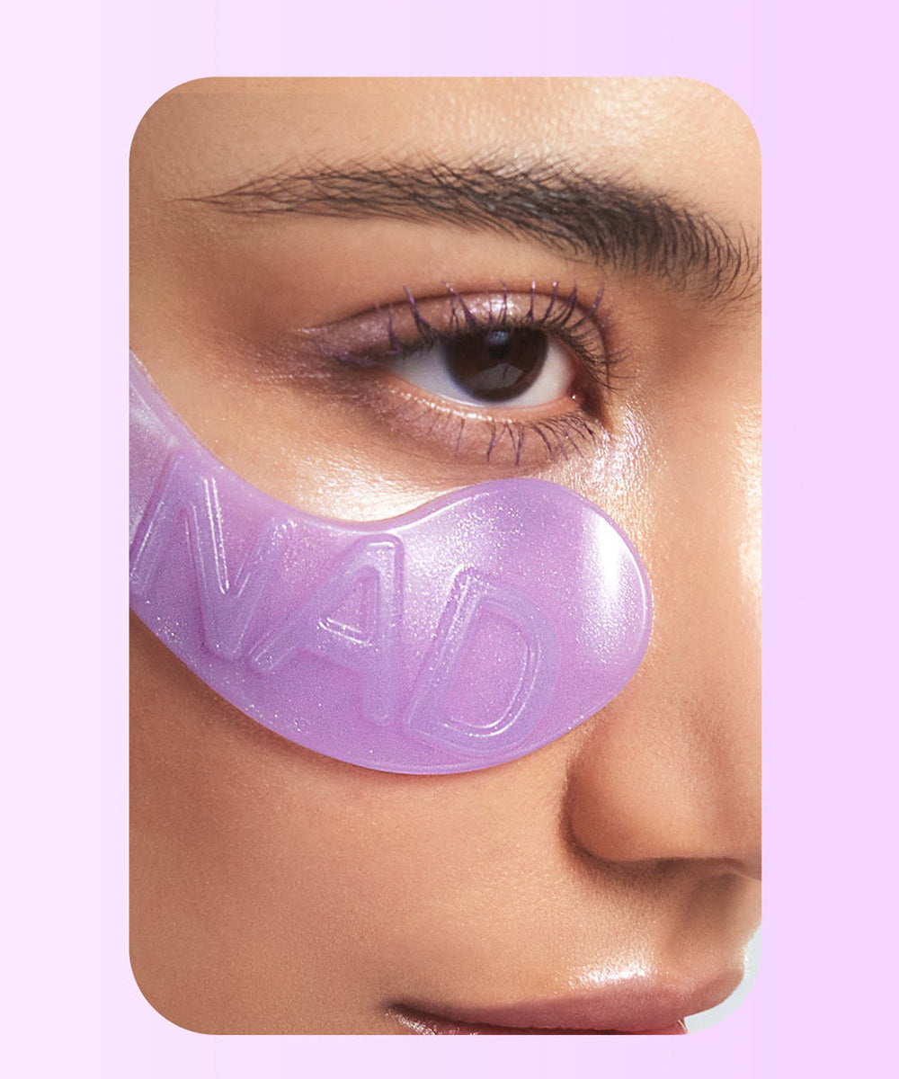 Close-up of a person wearing a purple eye mask with 'NAD' branding on a pink background.