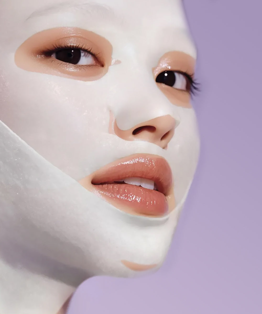 Close-up of a person wearing a white face mask against a light purple background